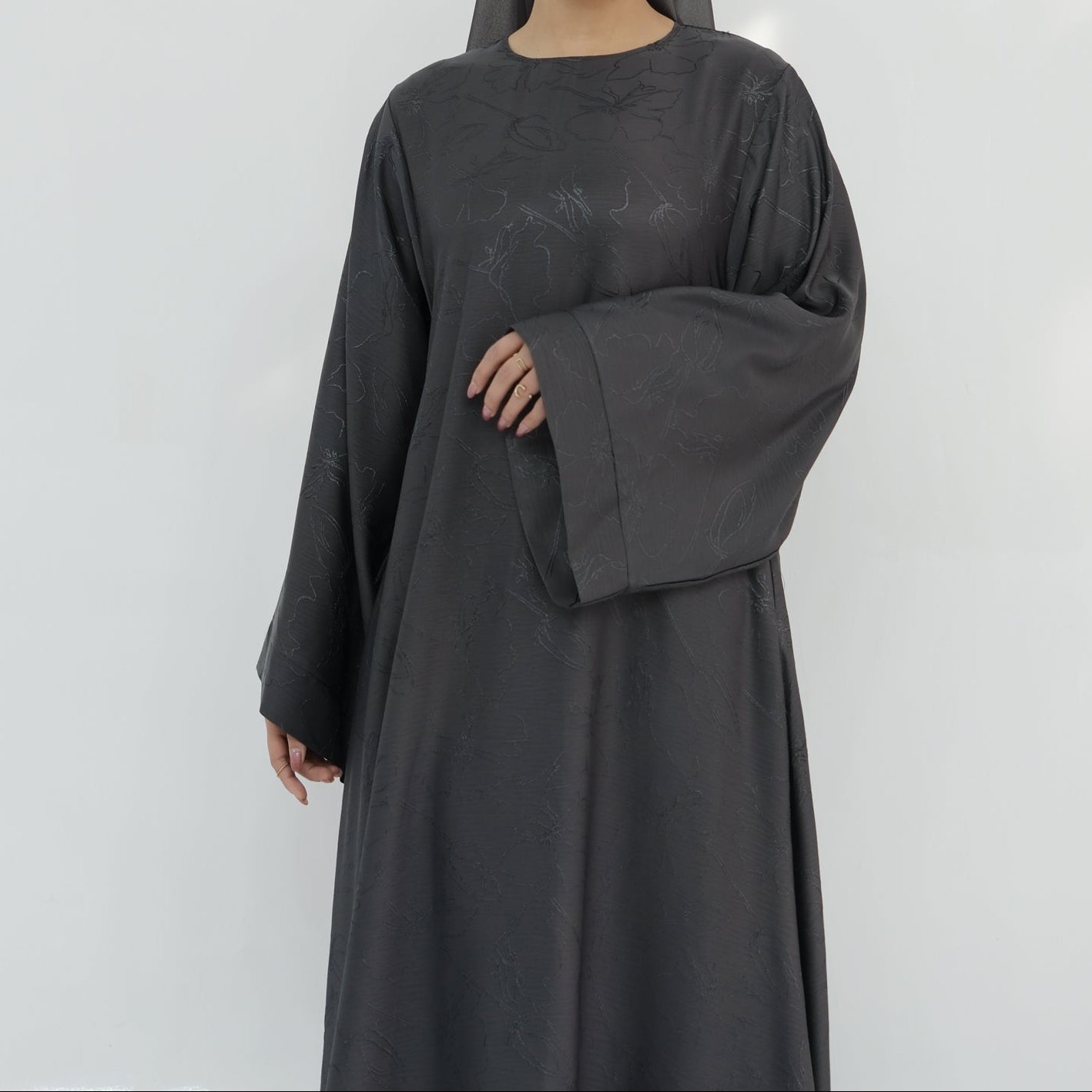 Woman wearing a dark gray abaya and matching hijab on a white background