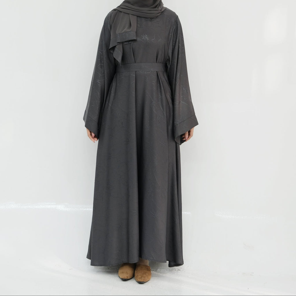 Person wearing a long dark gray dress with a hood against a white background