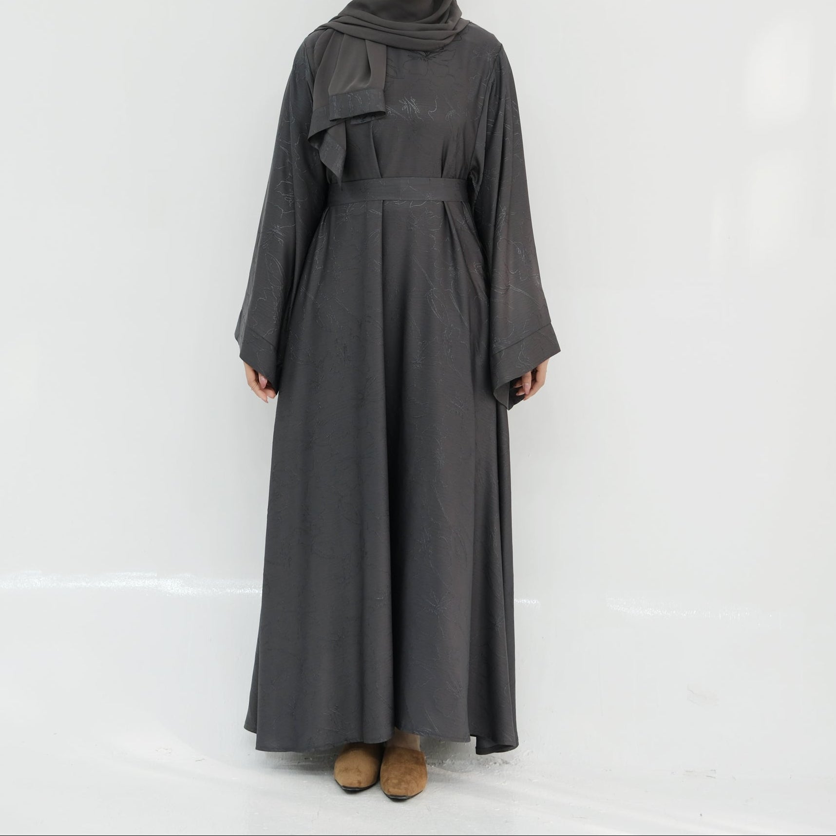 Person wearing a long dark gray dress with a hood against a white background