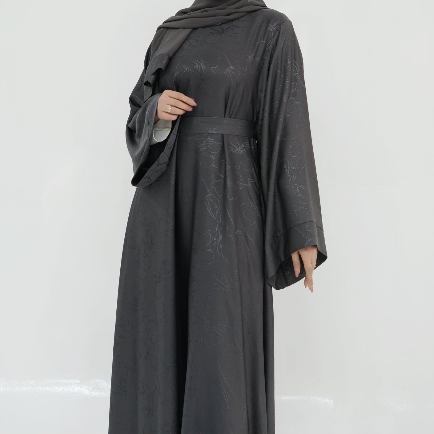 Woman wearing a dark gray abaya and hijab on a white background