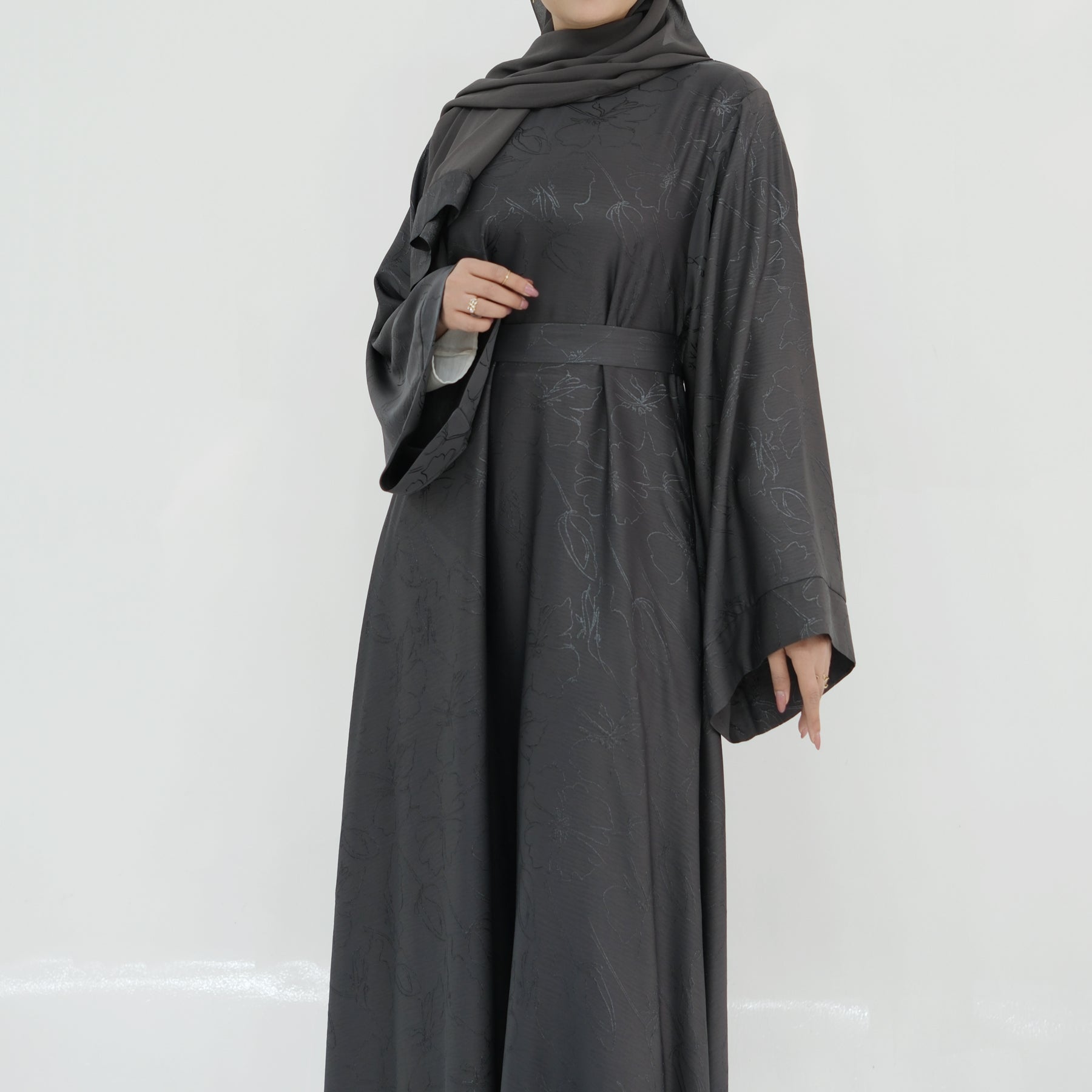 Person wearing a long dark gray dress with a matching hijab on a white background