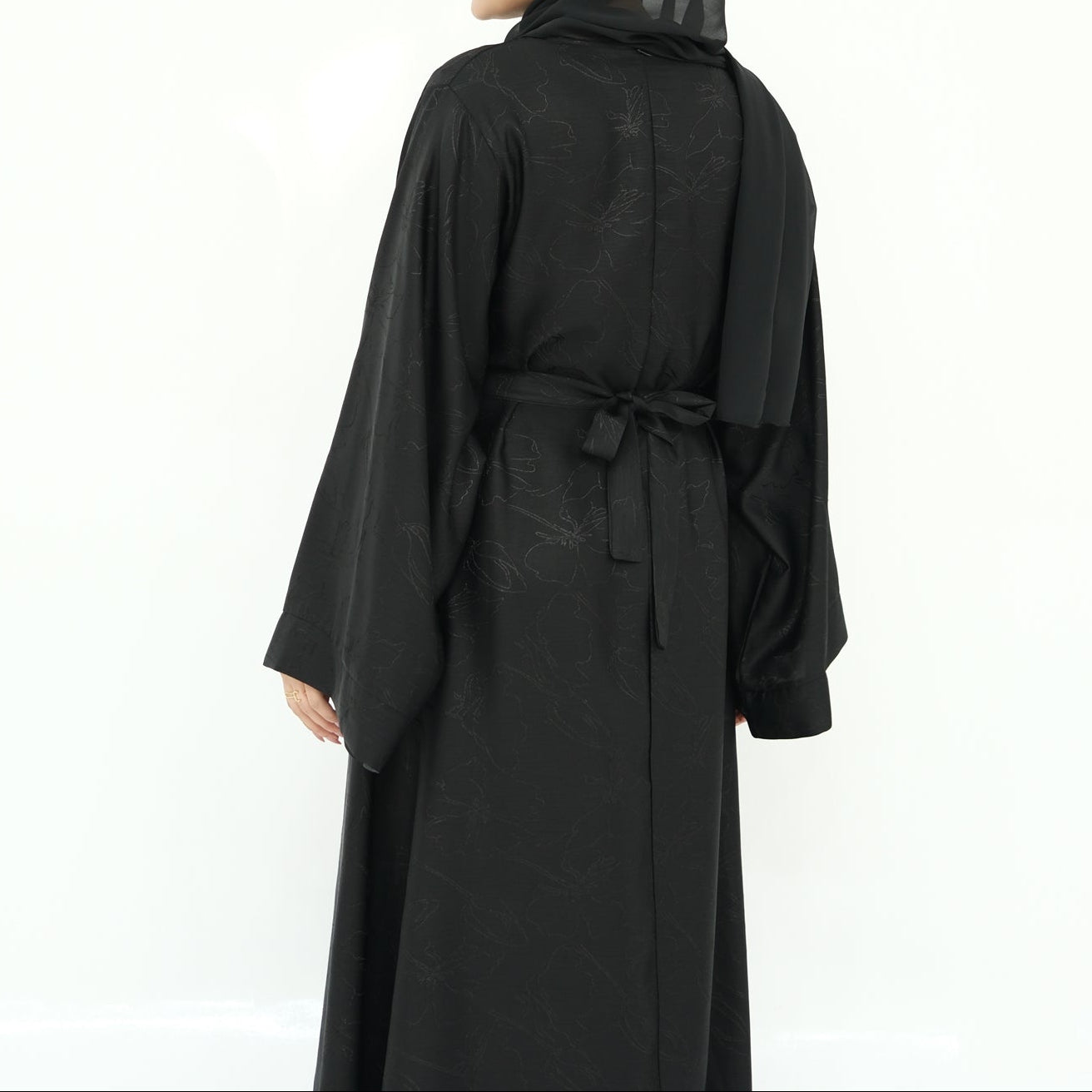 Woman wearing a black abaya and headscarf on a white background