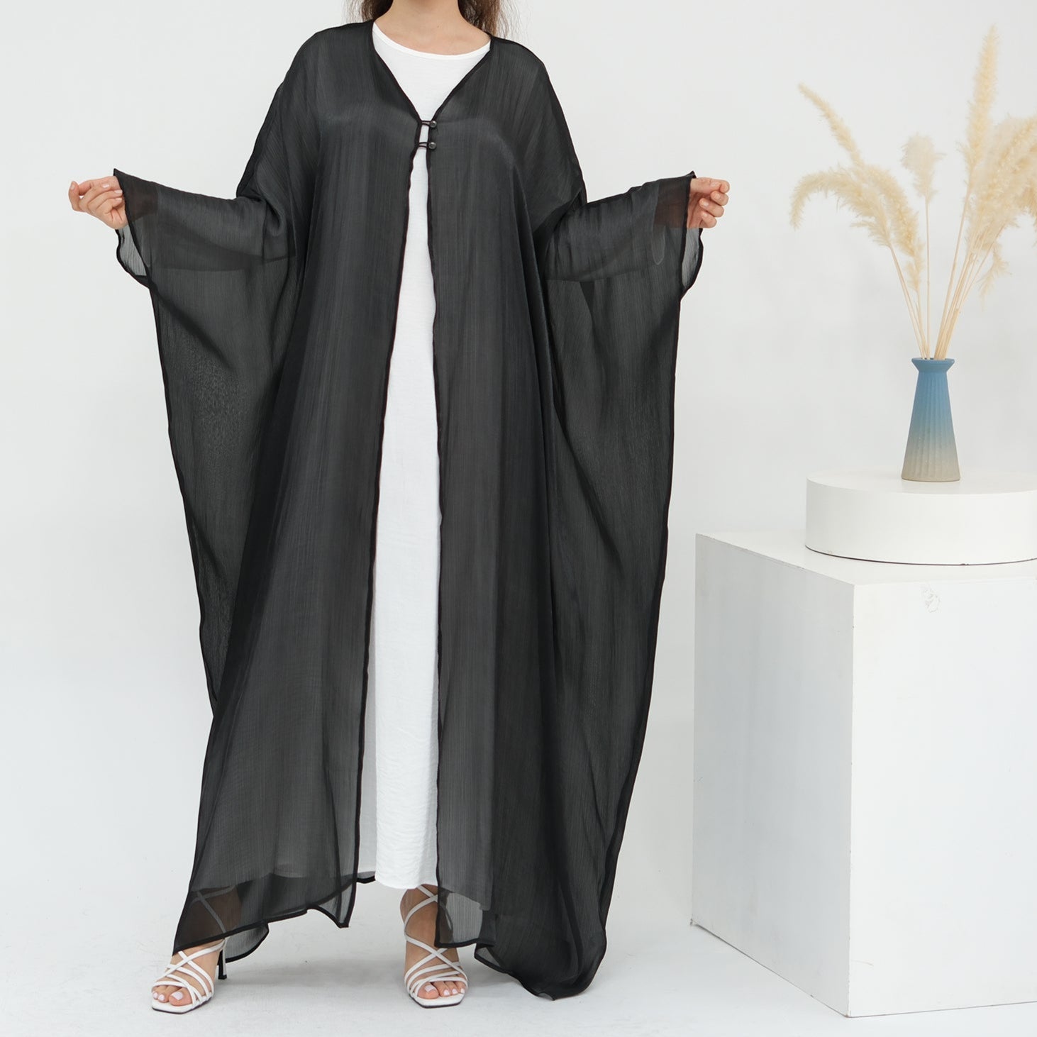 Woman wearing a black abaya over a white dress on a white background LayalAl-FajrAbaya_Noor_GraceBlack1