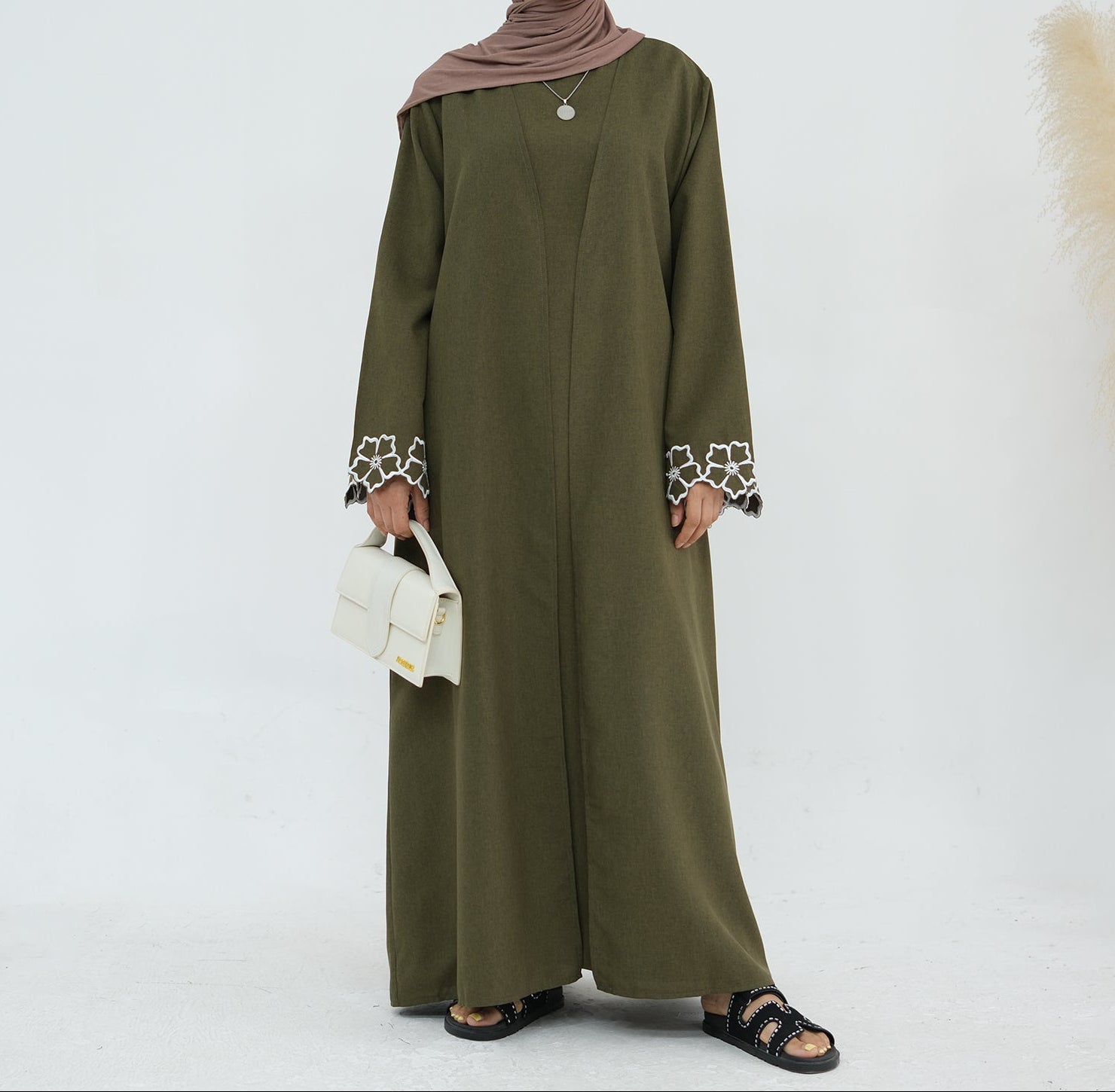 Person wearing an olive green abaya with white embroidery on a white background. Laylat Al-Qamar Abaya (عباءة ليلة القمر) - Noor & Grace