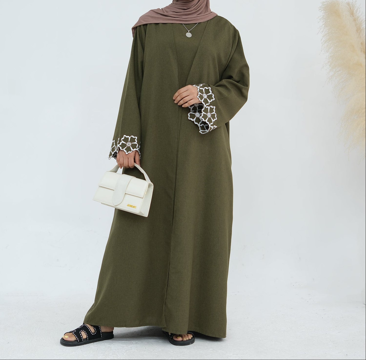Person wearing an olive green abaya with white embroidery on a white background. Laylat Al-Qamar Abaya (عباءة ليلة القمر) - Noor & Grace