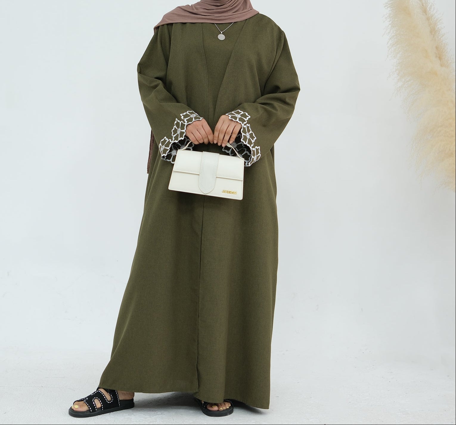Person wearing an olive green abaya with white embroidery on a white background. Laylat Al-Qamar Abaya (عباءة ليلة القمر) - Noor & Grace