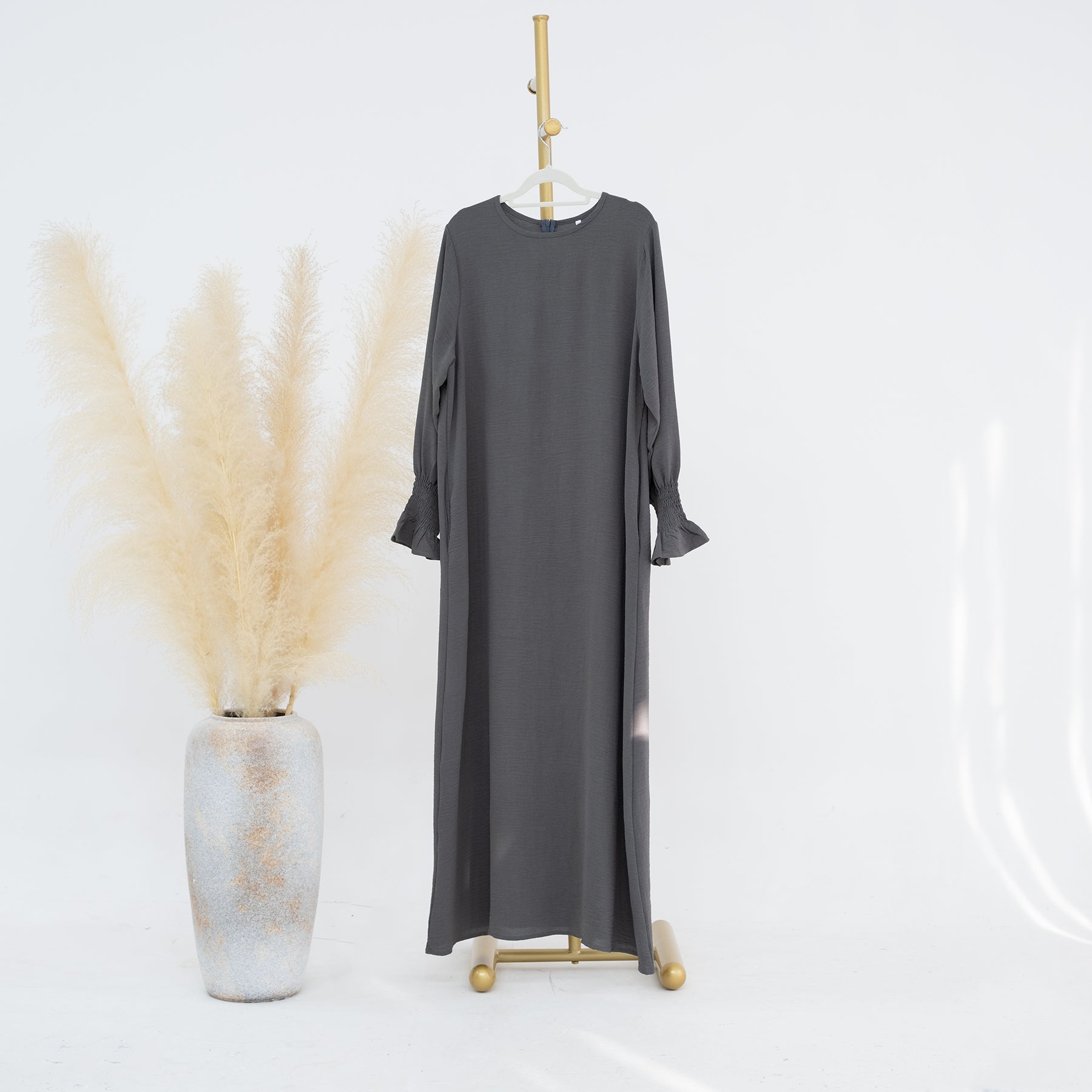 Gray long dress on a mannequin with a white background and decorative plant.