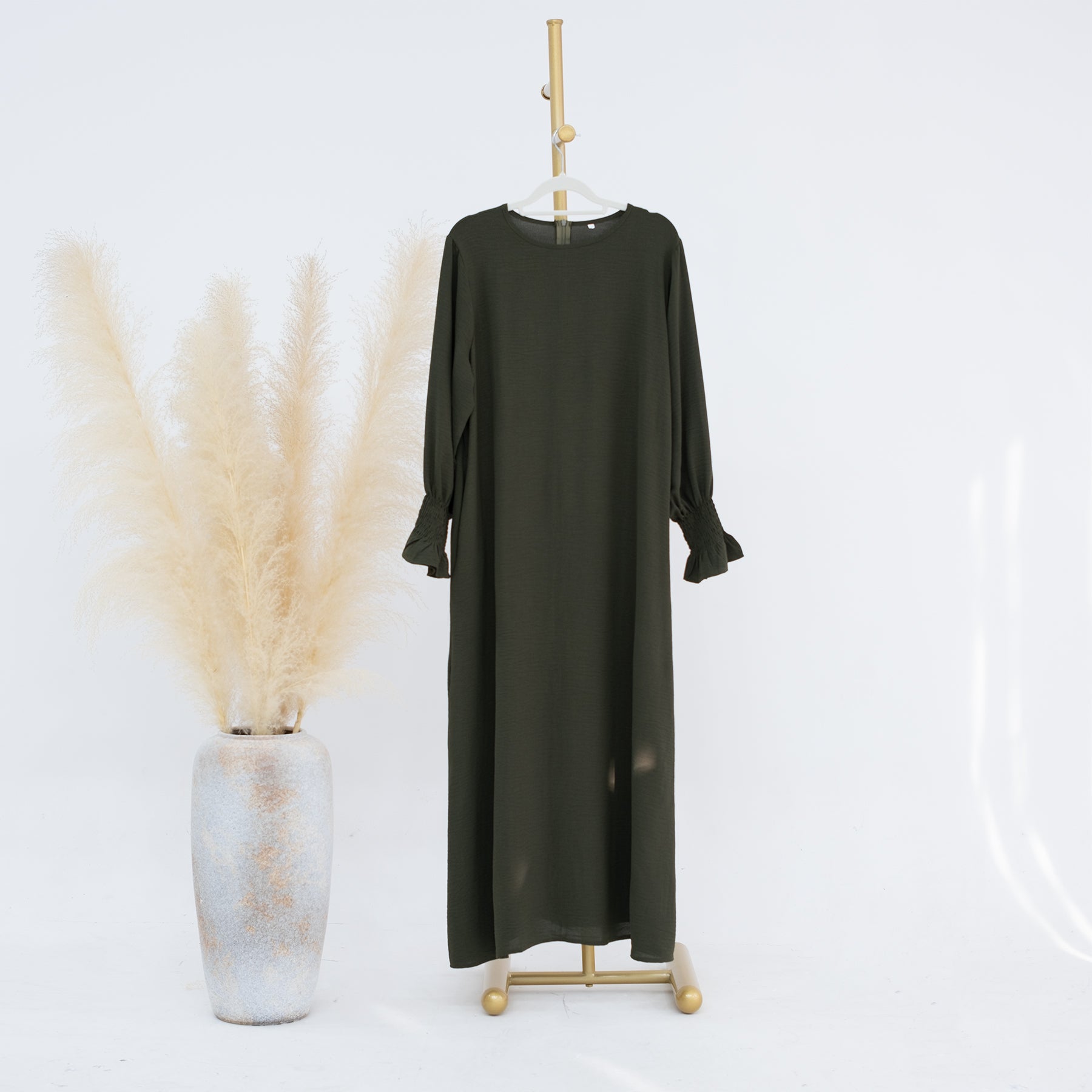 Black dress on a hanger with a white vase and dried plants on a light gray background