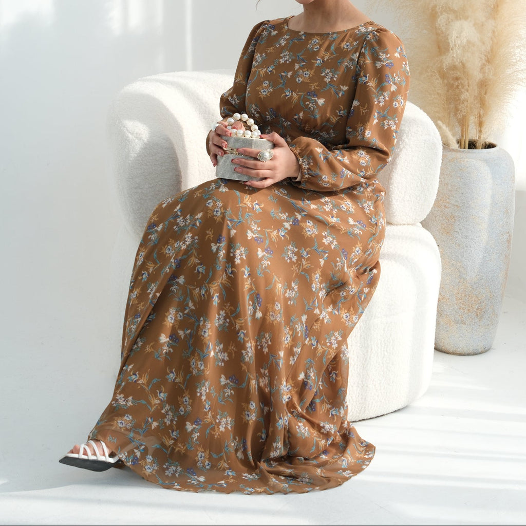 Woman in a long brown floral dress sitting on a white chair holding a bowl.