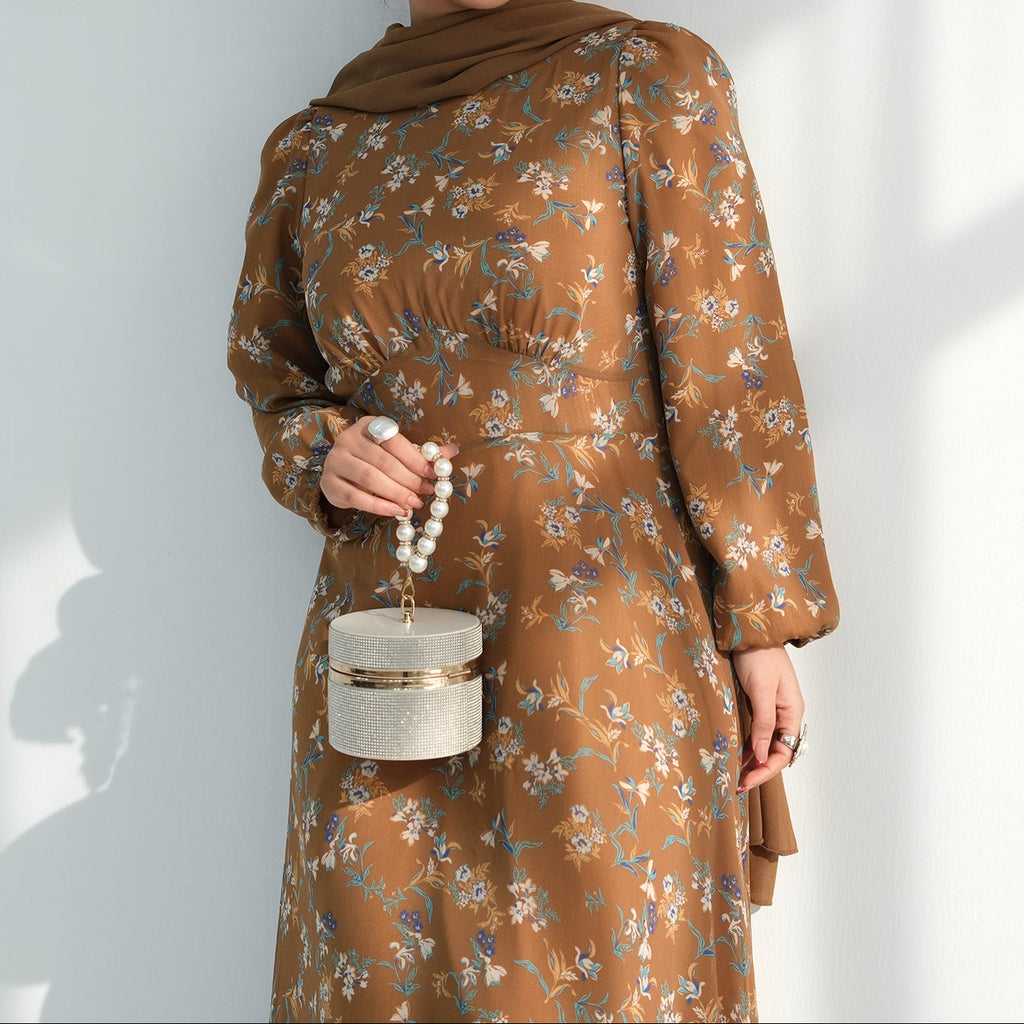 Woman wearing a brown floral dress holding a small white handbag against a light background