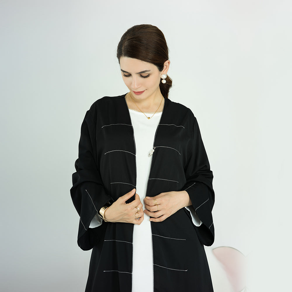Woman wearing a black abaya with white accents on a plain background