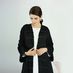 Woman wearing a black abaya with white accents on a plain background