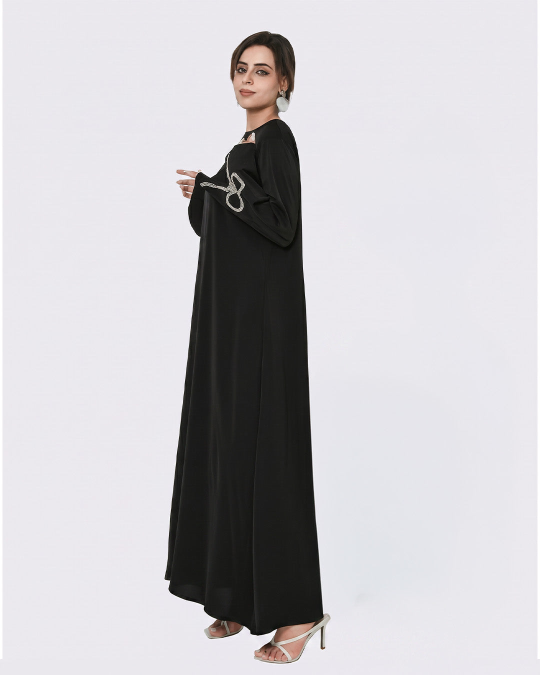 Woman wearing a black abaya with silver embroidery on a white background