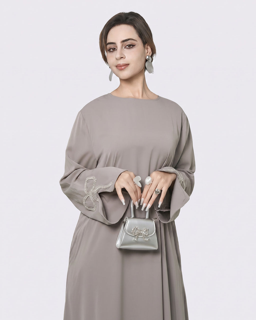 Woman wearing a gray dress holding a silver handbag against a white background