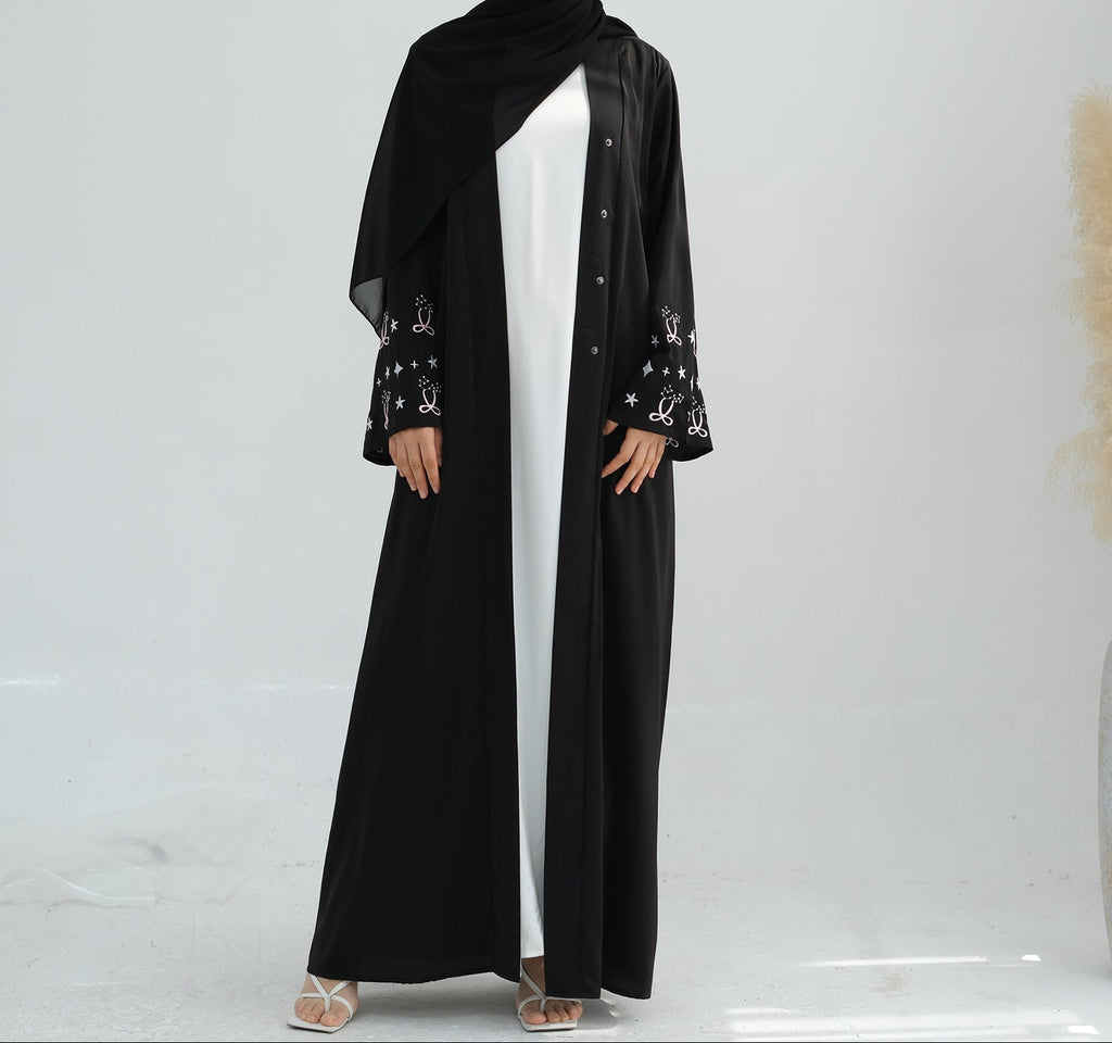 Woman wearing a black abaya with star patterns on a white background. Zina_Embroidered_Abaya_Noor & Grace