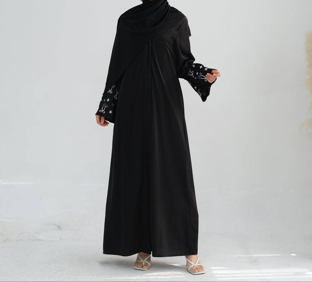 Woman wearing a black abaya with star patterns on a white background. Zina_Embroidered_Abaya_Noor & Grace