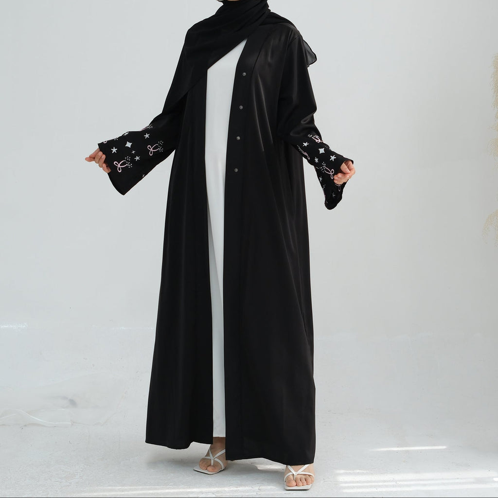 Woman wearing a black abaya with star patterns on a white background. Zina_Embroidered_Abaya_Noor & Grace