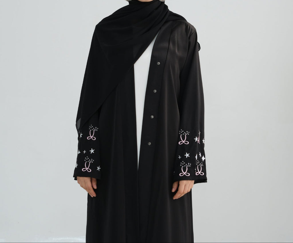 Woman wearing a black abaya with star patterns on a white background. Zina_Embroidered_Abaya_Noor & Grace