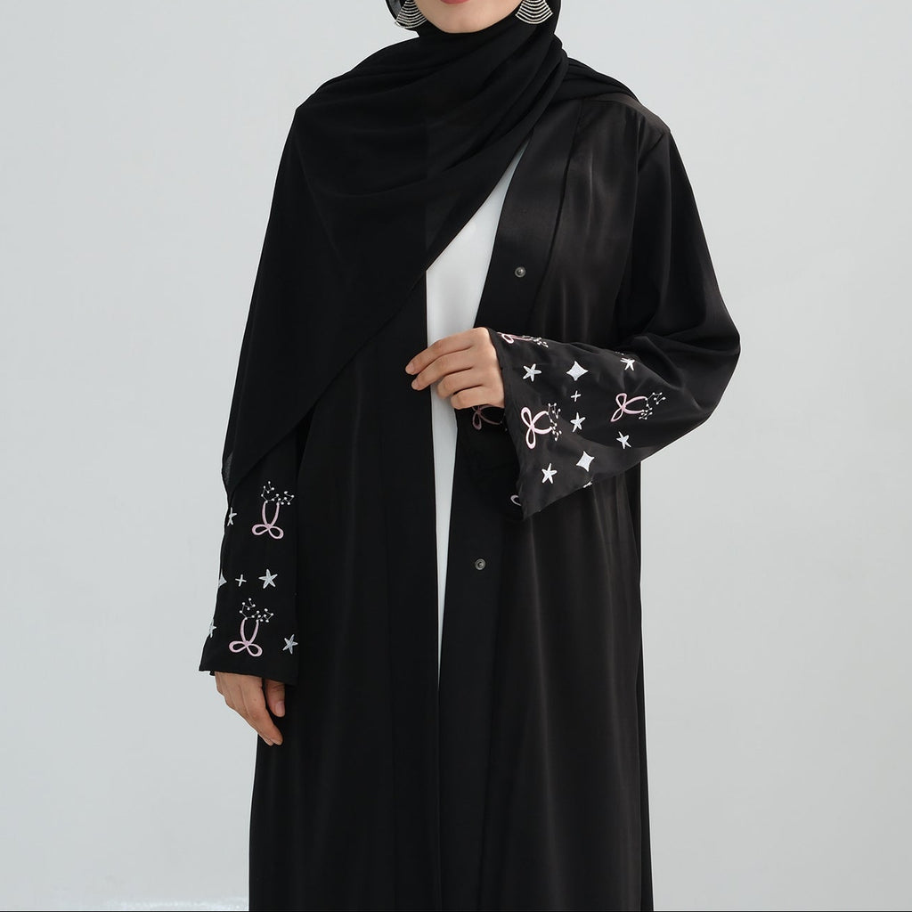 Woman wearing a black abaya with star patterns on a white background. Zina_Embroidered_Abaya_Noor & Grace