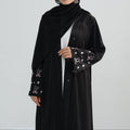 Woman wearing a black abaya with star patterns on a white background. Zina_Embroidered_Abaya_Noor & Grace