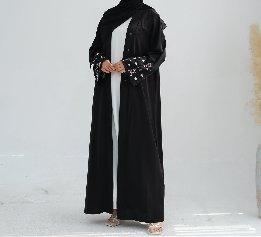 Woman wearing a black abaya with star patterns on a white background. Zina_Embroidered_Abaya_Noor & Grace