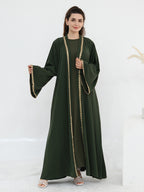 A woman modeling a dark green abaya dress with wide bell sleeves and gold chain trim along the front opening, shown against a clean white studio background.