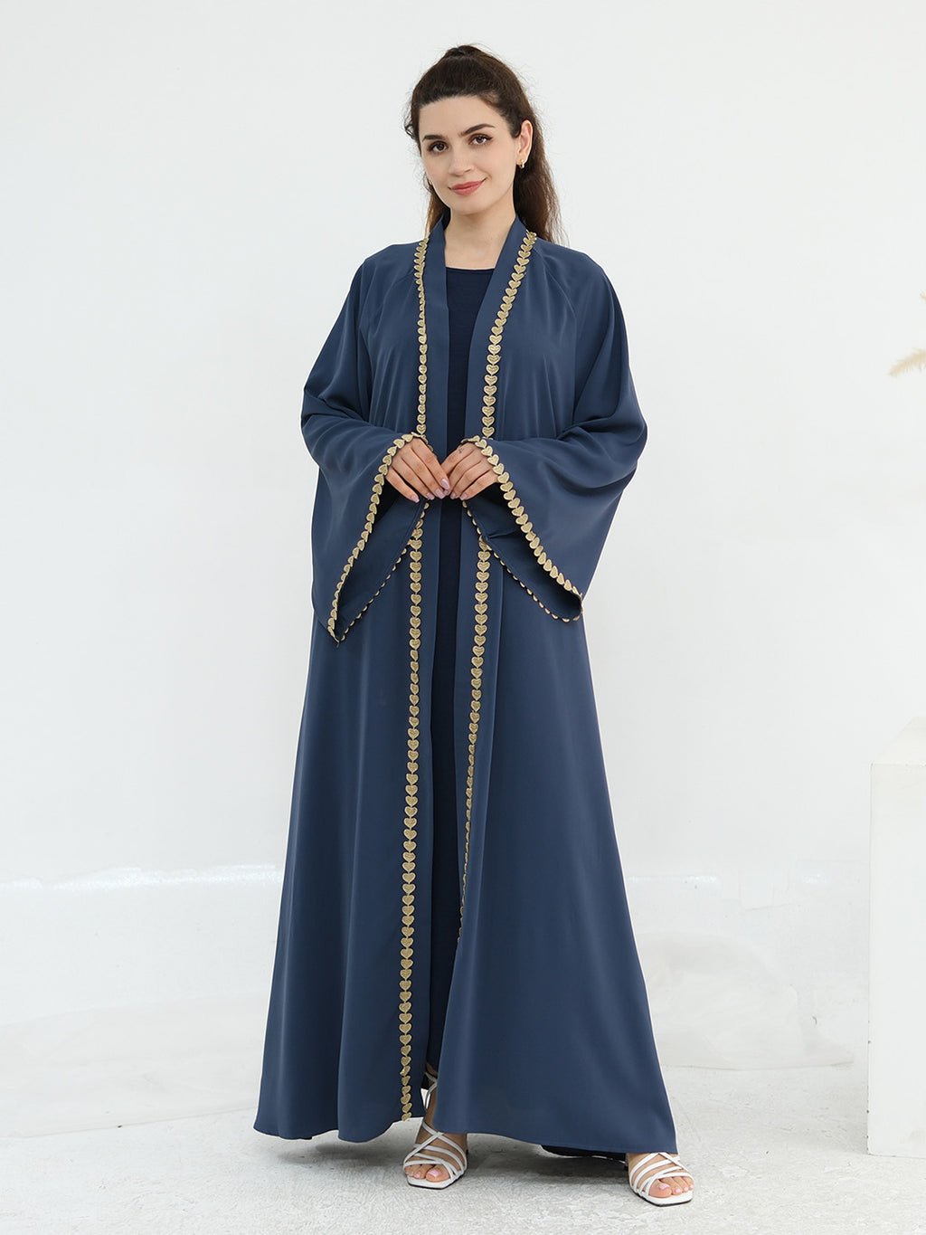 A woman modeling a navy blue abaya with gold embroidered trim along the edges, standing against a plain white studio background.