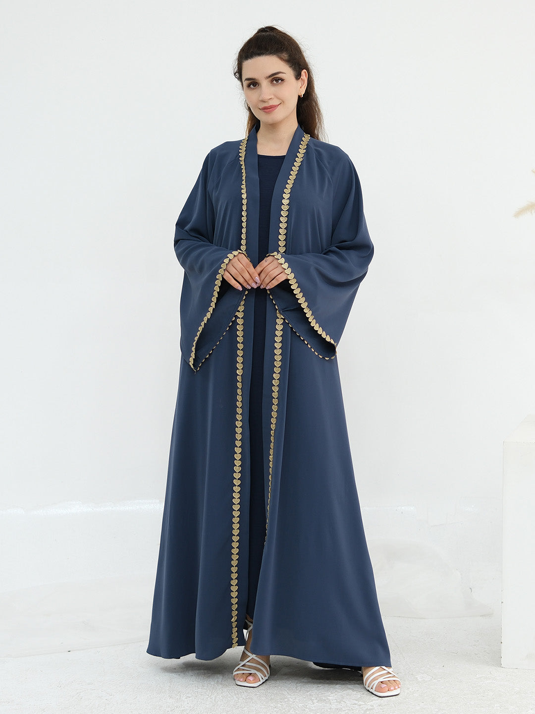 A woman modeling a navy blue abaya with gold embroidered trim along the edges, standing against a plain white studio background.