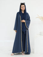A woman modeling a navy blue abaya set with a matching headscarf, featuring gold embroidered trim down the front, on a clean white studio background.
