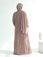 A woman wearing a dusty rose abaya and matching hijab, shown from the back. The abaya features small white embroidered details scattered across the fabric.