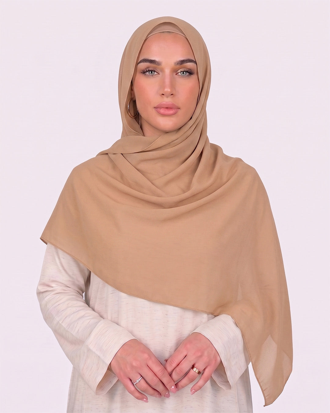 Model wearing a lightweight, bare chiffon hijab wrapped elegantly over a beige long-sleeved dress.