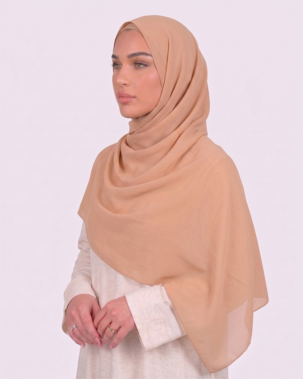 Model wearing a lightweight, bare chiffon hijab wrapped elegantly over a beige long-sleeved dress.