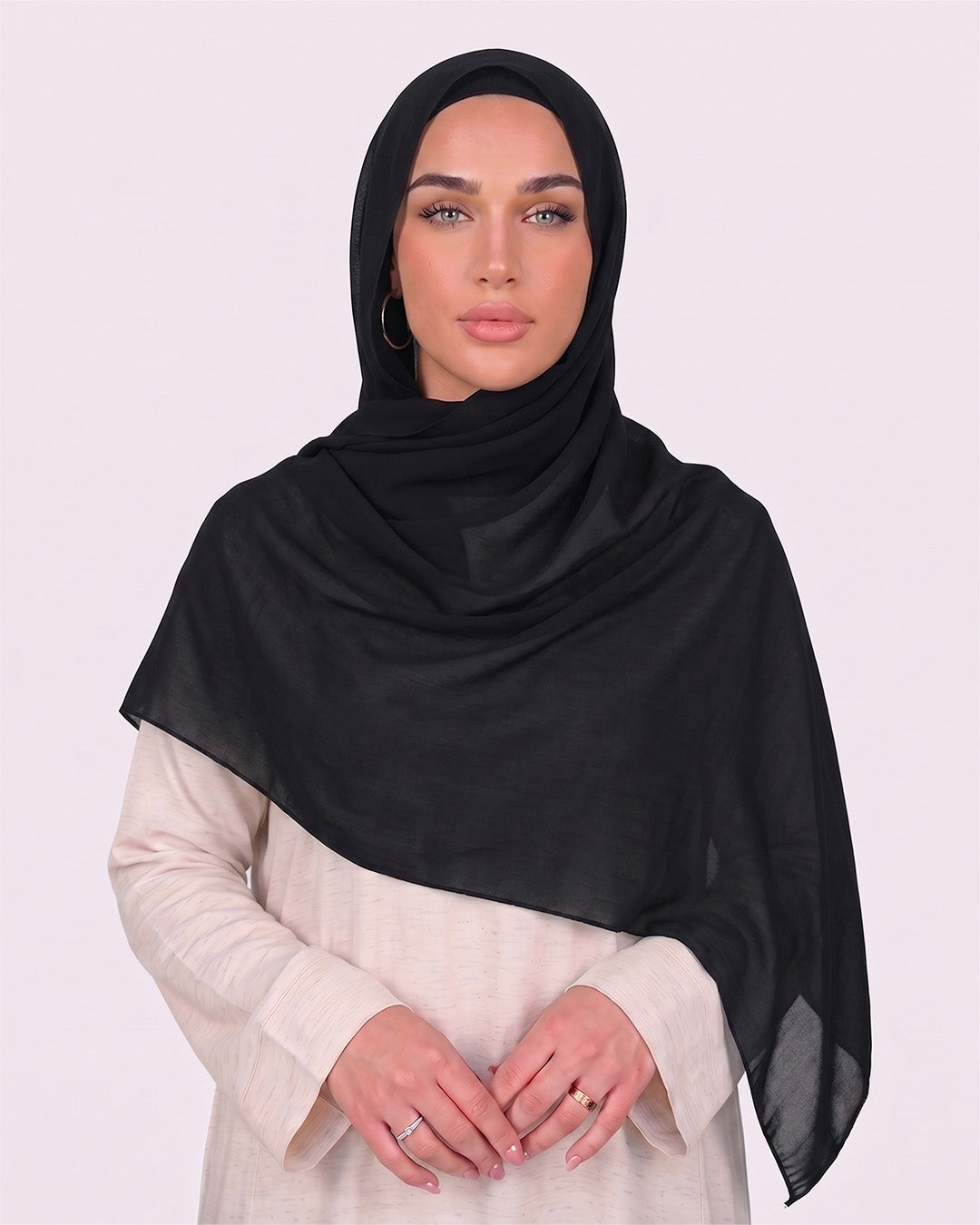 Model wearing a lightweight, black chiffon hijab wrapped elegantly over a beige long-sleeved dress.
