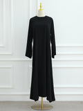 A long-sleeve black maxi dress displayed on a cream dress form with a gold finial and stand, set against a white paneled wall.