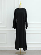 A long-sleeve black maxi dress displayed on a cream dress form with a gold finial and stand, set against a white paneled wall.