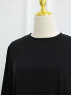 A black long-sleeve top displayed on a cream dress form with a gold neck cap against a plain white background.