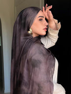 A woman in profile wearing a sheer, dark plum hijab and a light beige long-sleeve top, with a large gold earring visible.