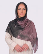 A woman wearing a moody black and dusty mauve printed modal hijab with a watercolor tie-dye texture, paired with a cream shirt dress.