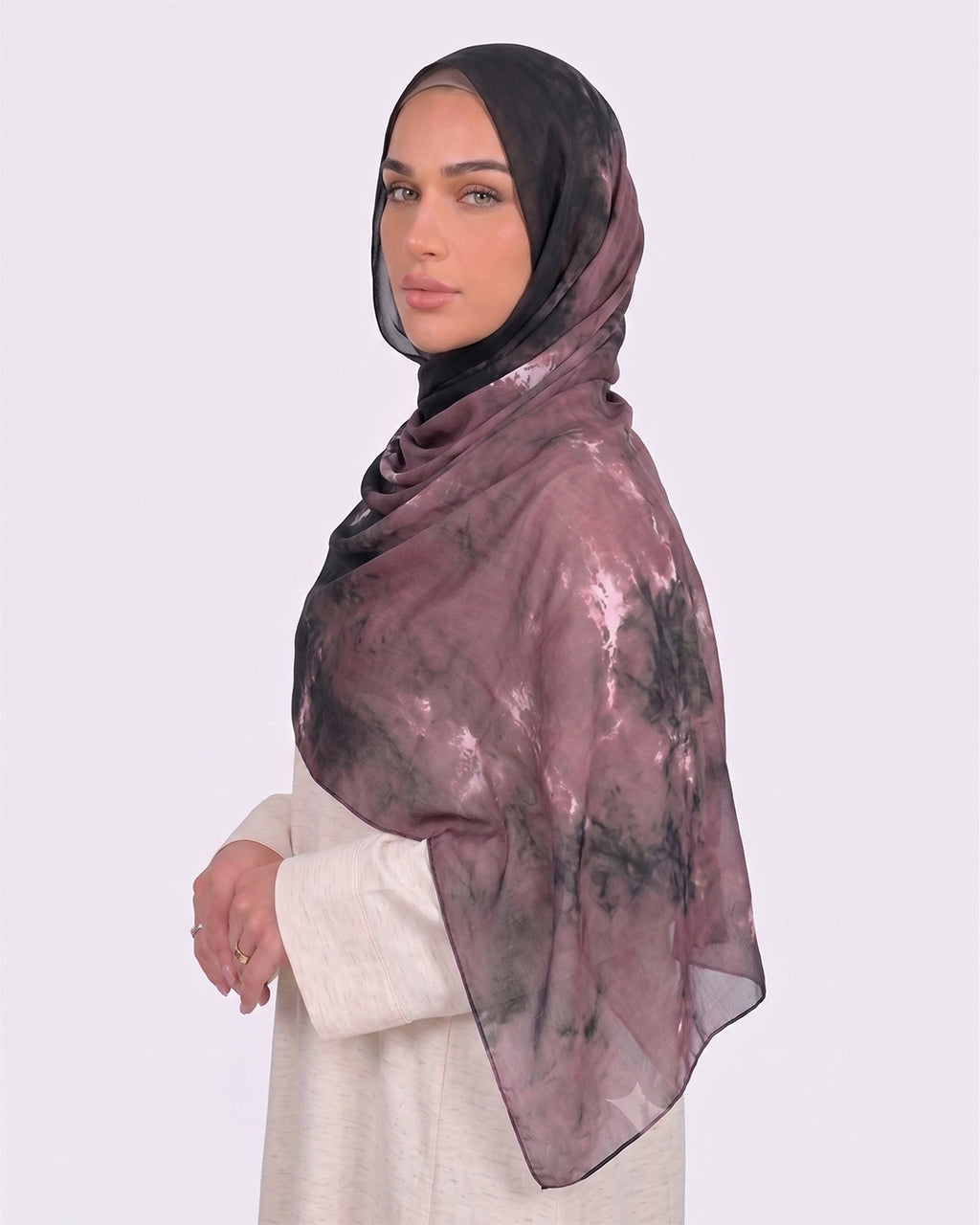 A woman wearing a moody black and dusty mauve printed modal hijab with a watercolor tie-dye texture, paired with a cream shirt dress.