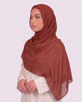 Model wearing a lightweight, brick red chiffon hijab wrapped elegantly over a beige long-sleeved dress.