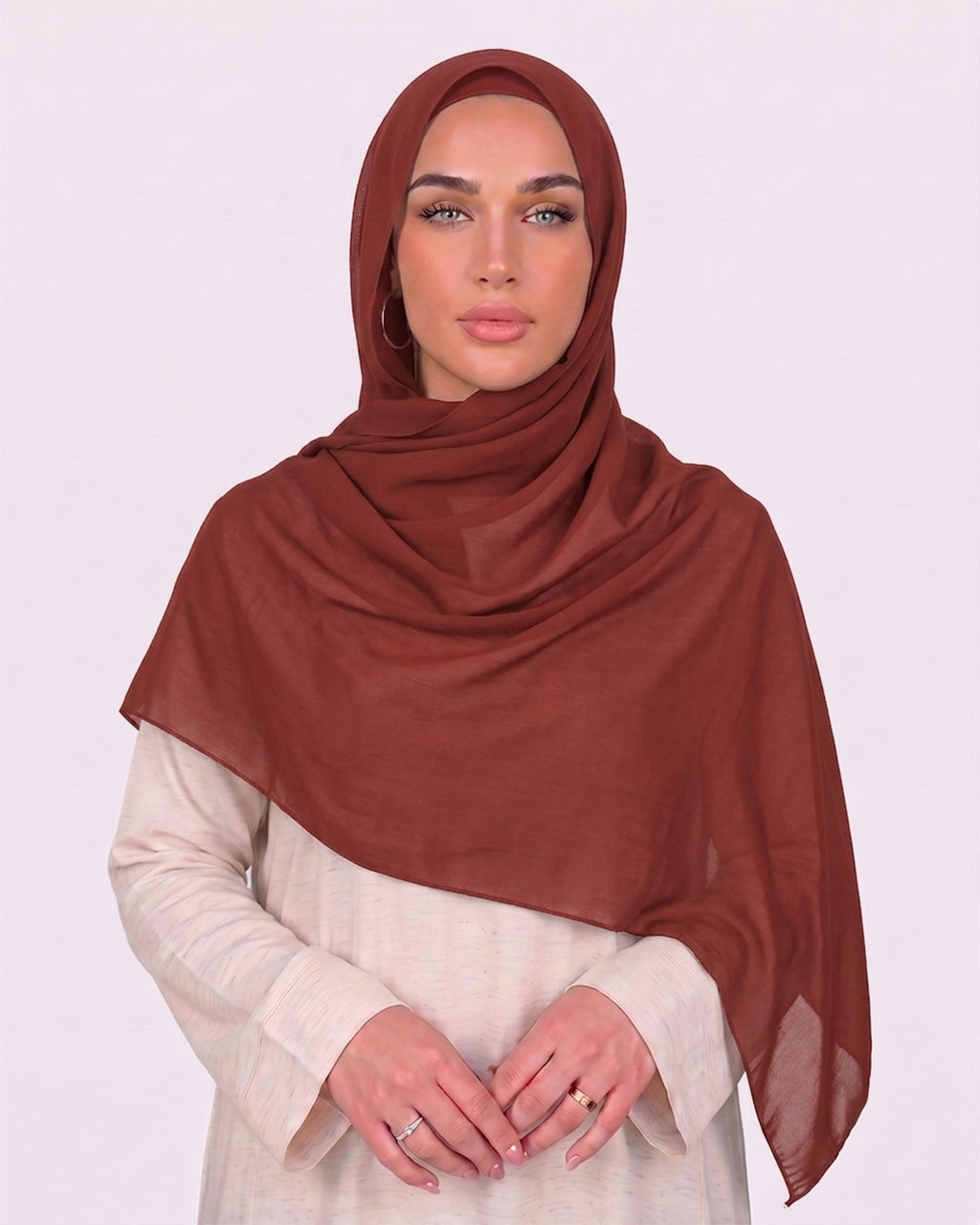 Model wearing a lightweight, brick red chiffon hijab wrapped elegantly over a beige long-sleeved dress.