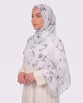 A woman wearing a classic white marble printed modal hijab with crisp black veining, paired with a minimalist cream-colored outfit.