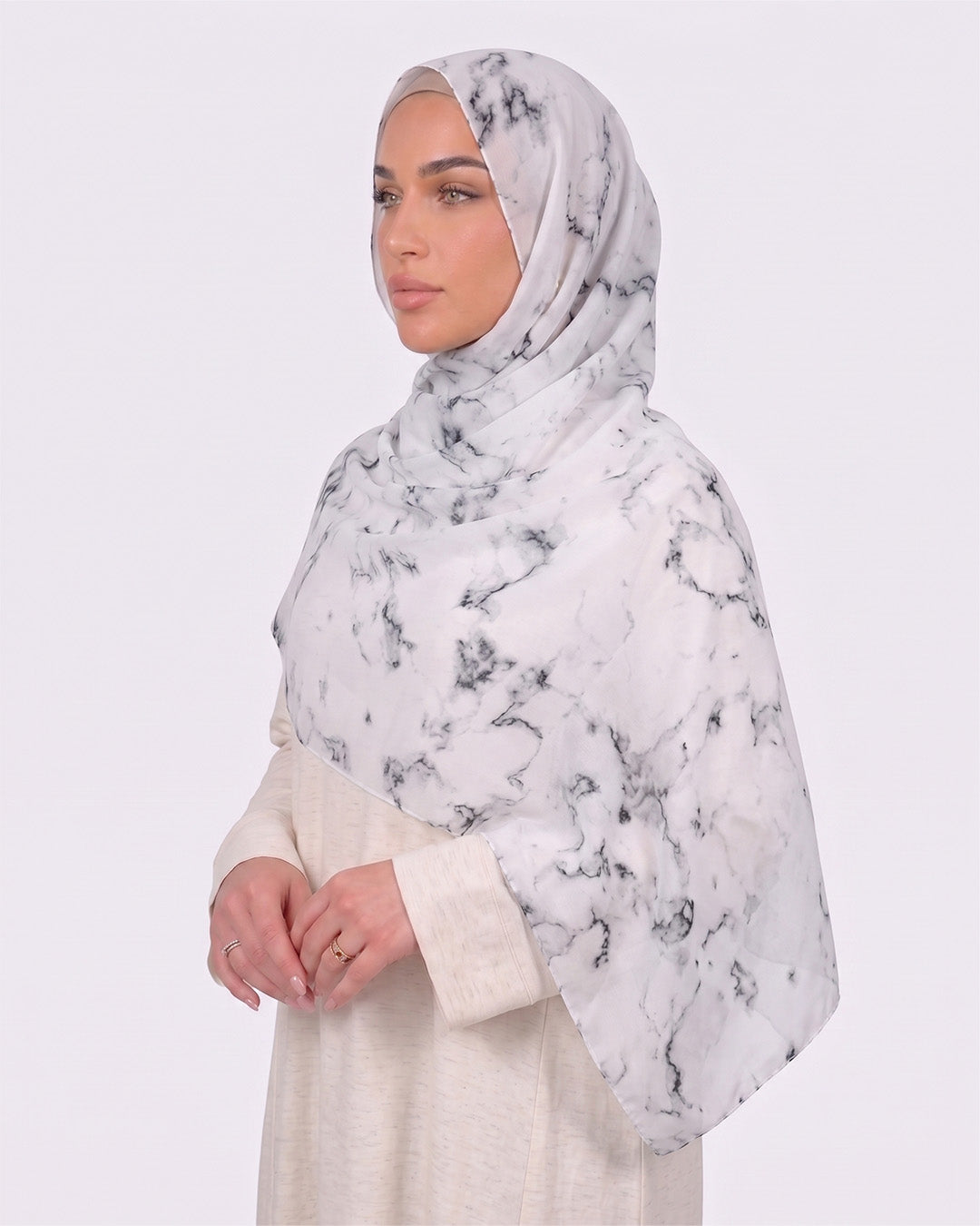 A woman wearing a classic white marble printed modal hijab with crisp black veining, paired with a minimalist cream-colored outfit.