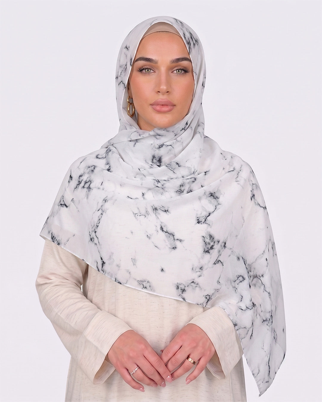 A woman wearing a classic white marble printed modal hijab with crisp black veining, paired with a minimalist cream-colored outfit.