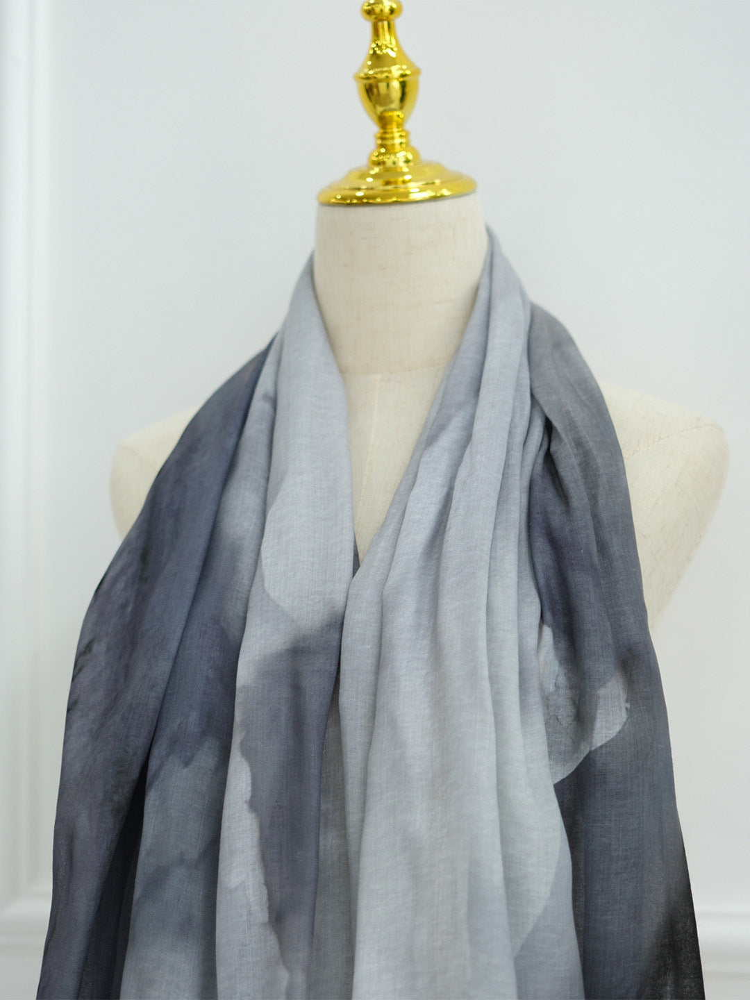 A lightweight gradient scarf draped on a cream-colored mannequin torso with a gold finial, set against a plain white background.