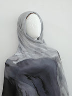 A lightweight sheer hijab or shawl draped on a white mannequin head, featuring a watercolor-like gradient from light gray at the top to dark charcoal gray at the bottom.