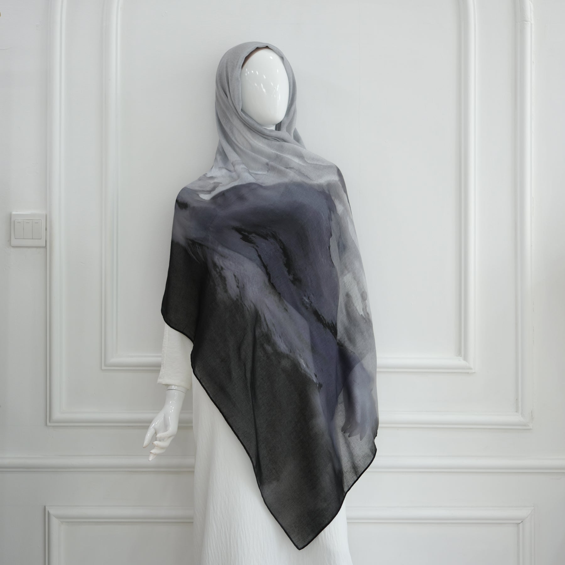 Mannequin wearing a black and gray scarf against a white paneled wall.