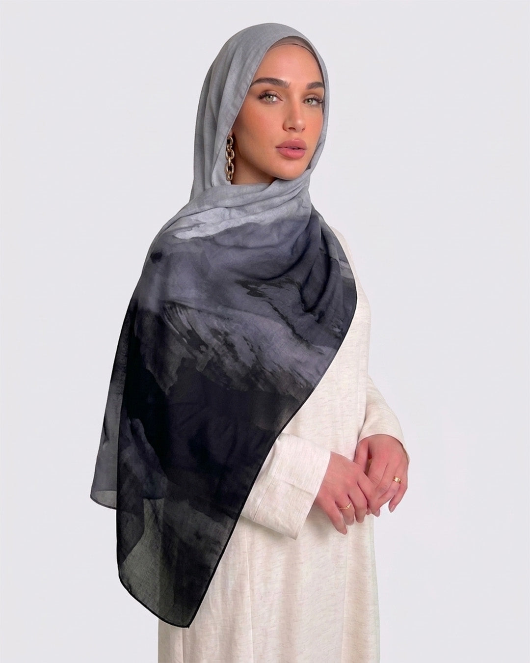 A woman wearing a modern monochrome ombré printed modal hijab that gradients from light grey to deep black, paired with a cream-colored dress
