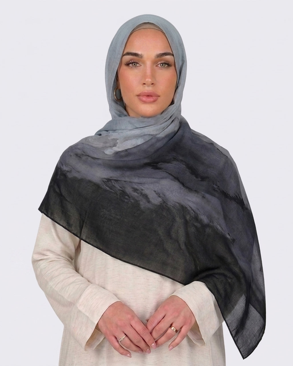 A woman wearing a modern monochrome ombré printed modal hijab that gradients from light grey to deep black, paired with a cream-colored dress