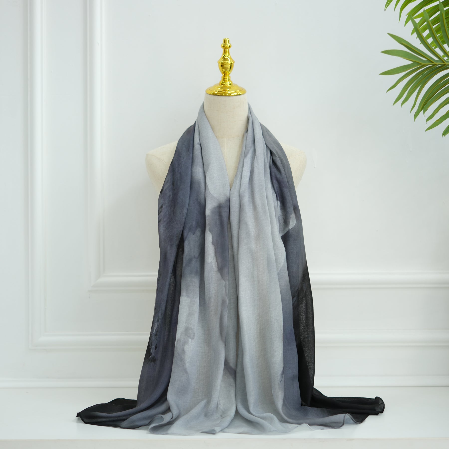 Gray gradient scarf on a mannequin against a white wall with a plant in the corner